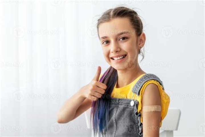 Cheerful Smiling Adolescent Patient Showing Vaccinated Arm With Sticking Patch On Her Shoulder After Getting Shot And Thumb Up Gesture.